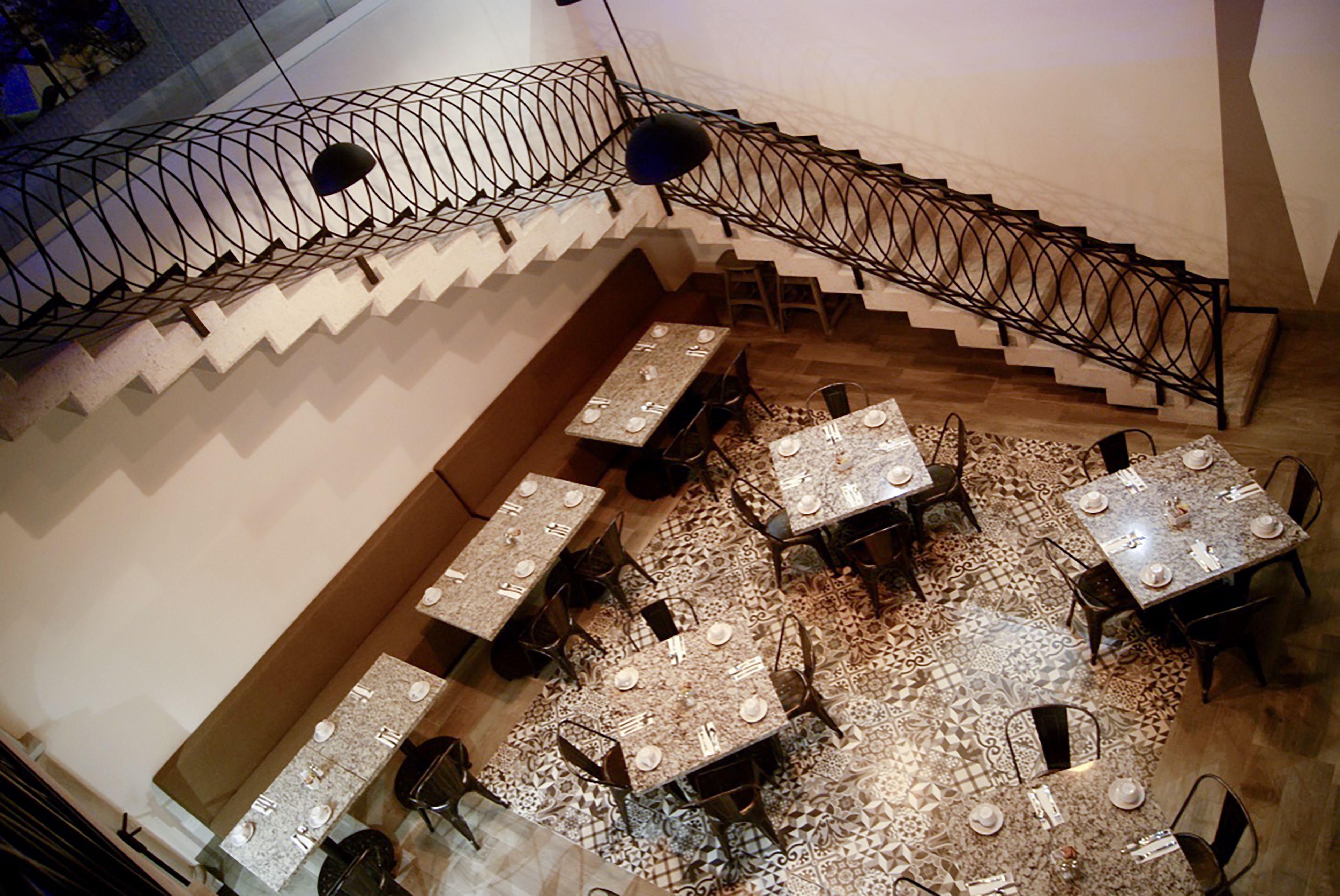 Ein Restaurant mit mehreren Tischen und Stühlen, einer Treppe mit Metallgeländer und einem gestreiften Boden.