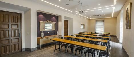 A conference room with long tables and chairs, a ceiling projector, and a wooden door.
