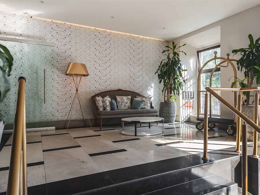 A modern lobby with a patterned wall, a sofa, a coffee table, and a staircase with a railing.