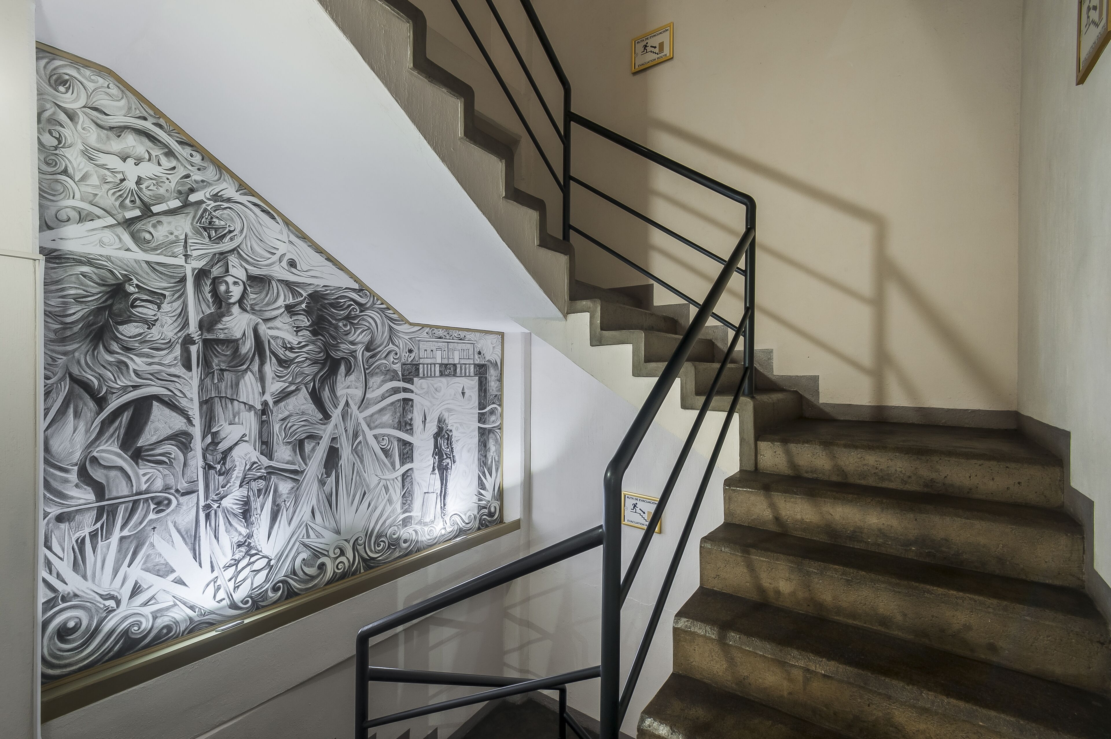 A staircase with a black metal railing and a detailed wall mural.