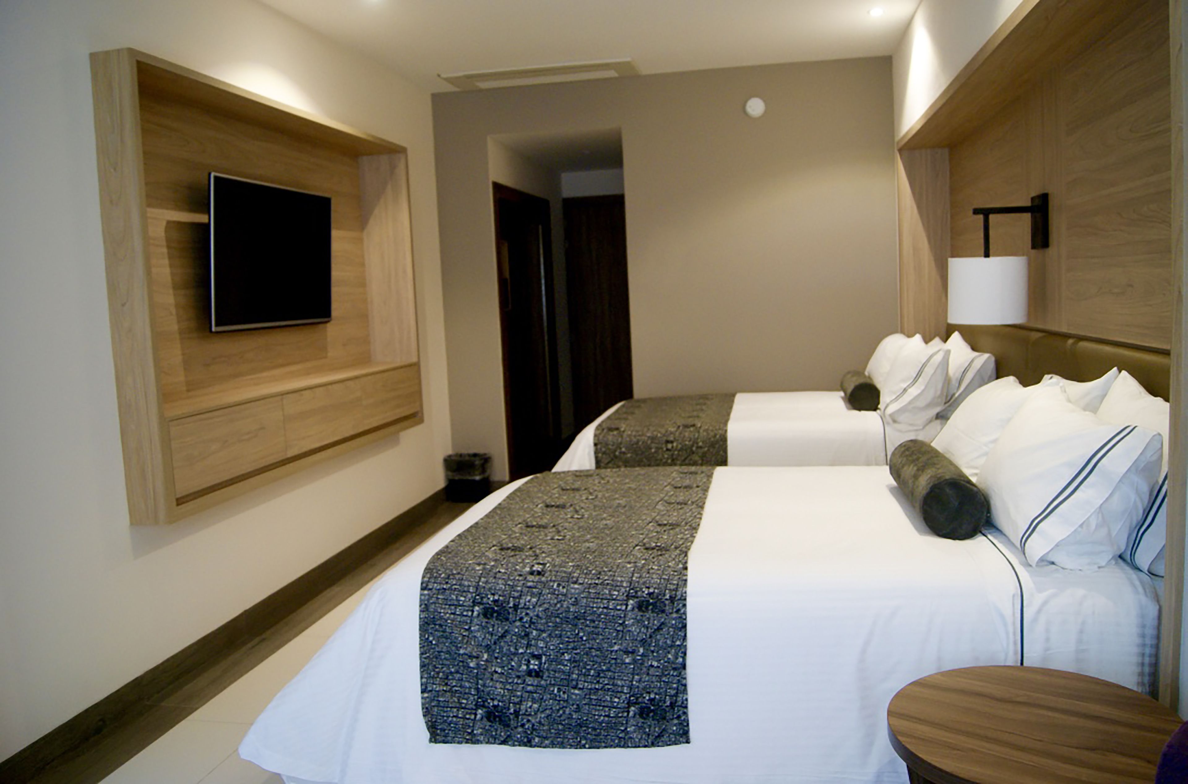 A hotel room with two beds, a flat-screen TV mounted on the wall, a wooden headboard, and a bedside table.