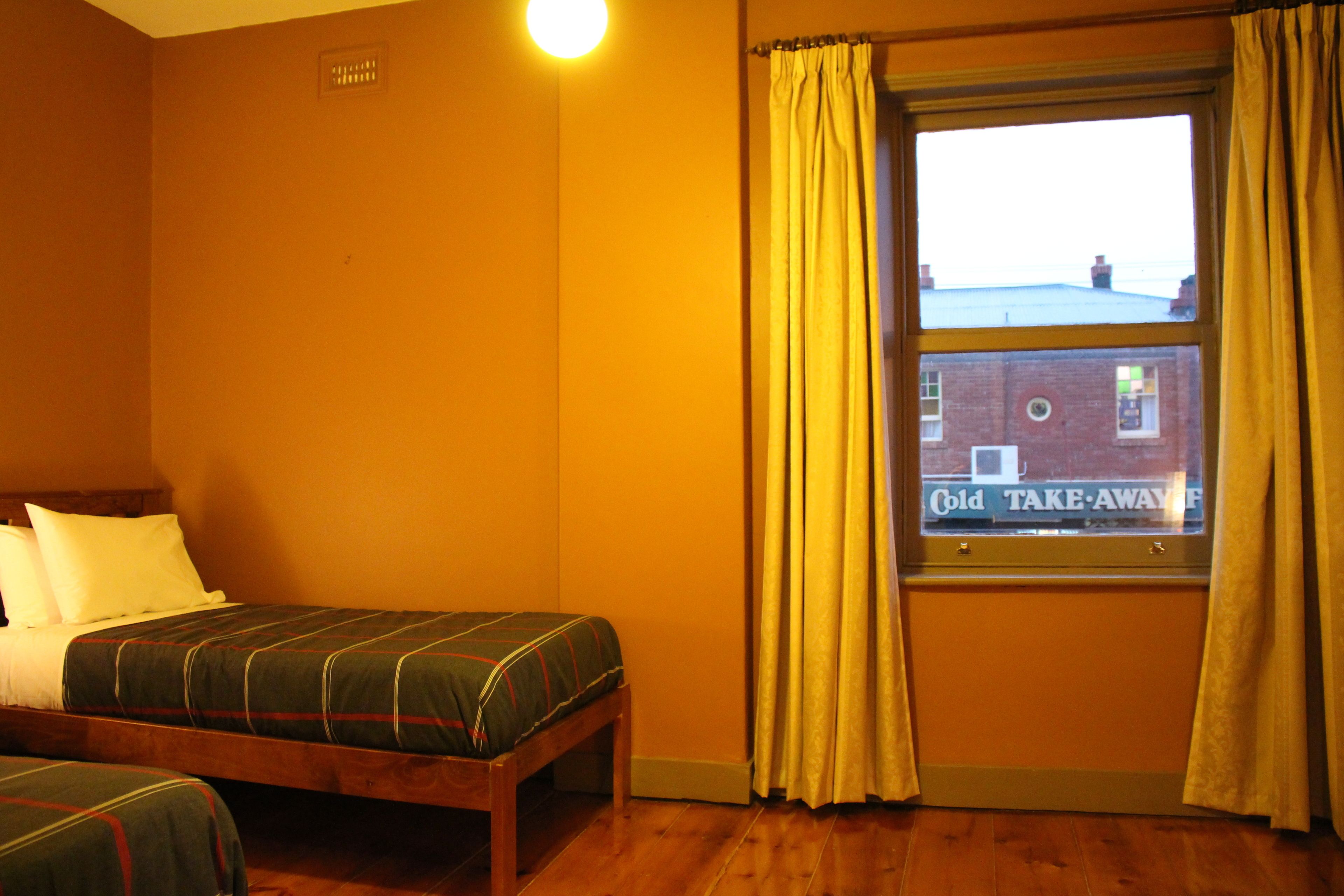 Une chambre avec deux lits simples, une fenêtre avec des rideaux et une vue sur un bâtiment à l’extérieur.