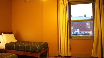 Une chambre avec deux lits simples, une fenêtre avec des rideaux et une vue sur un bâtiment à l’extérieur.