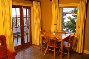 A dining area with a wooden table and chairs, a small potted plant, and a view through a glass door. - The Tasmanian Inn (Hobart)