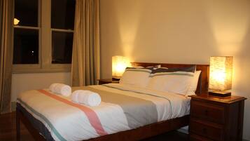 A neatly made bed with a wooden frame, two bedside tables with lamps, and a window with curtains.
