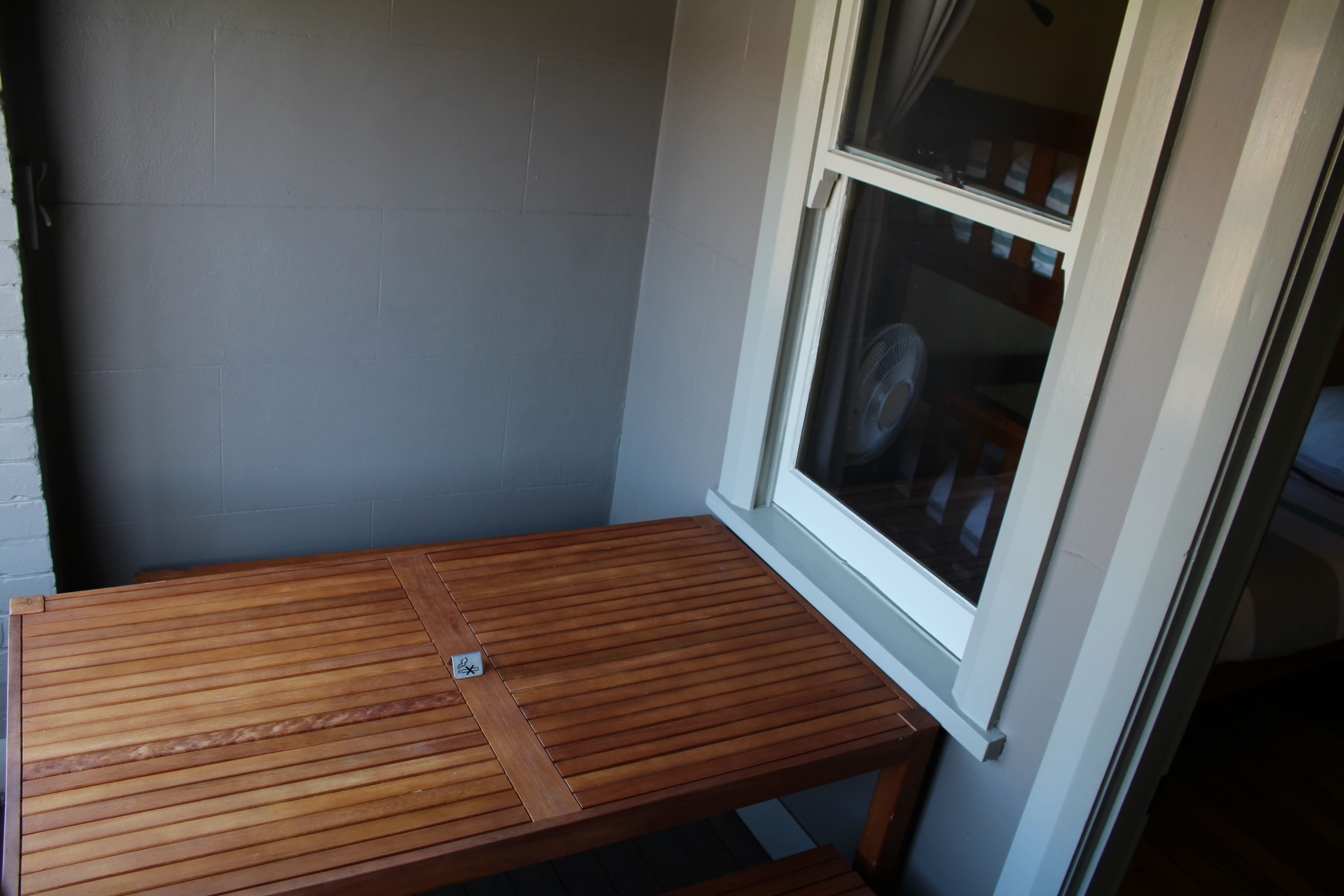 A small wooden table with a metal support in a corner of a room with a grey wall and a window.