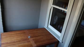 Een houten tafeltje met een metalen voet in een hoek van een kamer met een grijze muur en een raam.