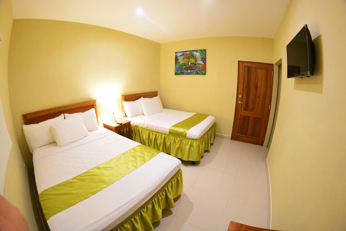 A hotel room with two beds, a television mounted on the wall, and a door.