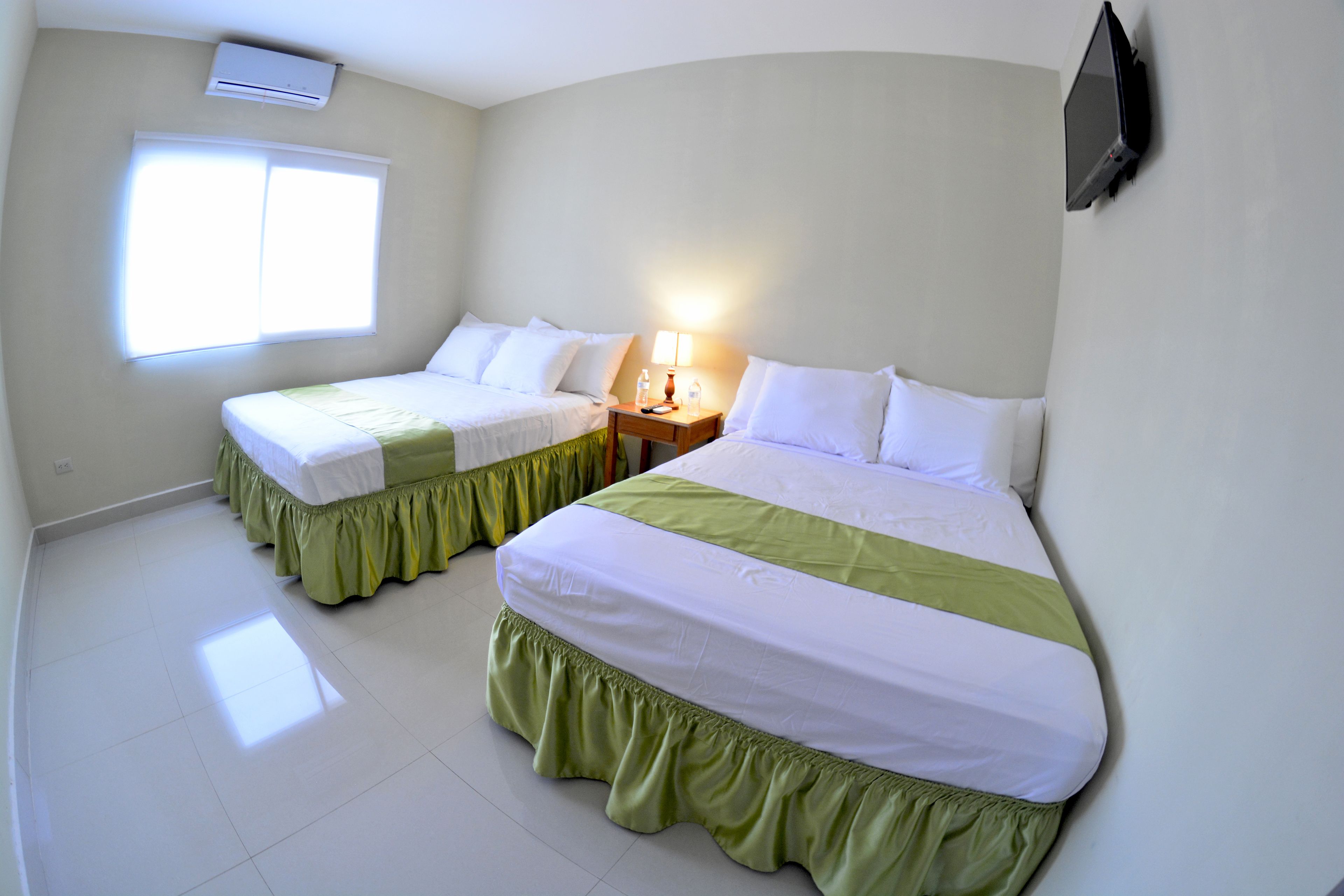 Habitación de hotel con dos camas, una ventana, una mesita de noche y un televisor instalado en la pared.