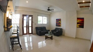 A spacious living area with a high ceiling, a ceiling fan, two black leather sofas, a glass coffee table, and a bar area with stools. - Hostal Santa Martha (Managua)