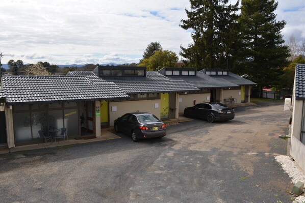 A building with a tiled roof, two cars parked in front, and a reception area with chairs outside.