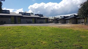 A row of single-story buildings with a flat roof, a grassy area in the foreground, and a clear sky with clouds. - The Apple Inn (Batlow)