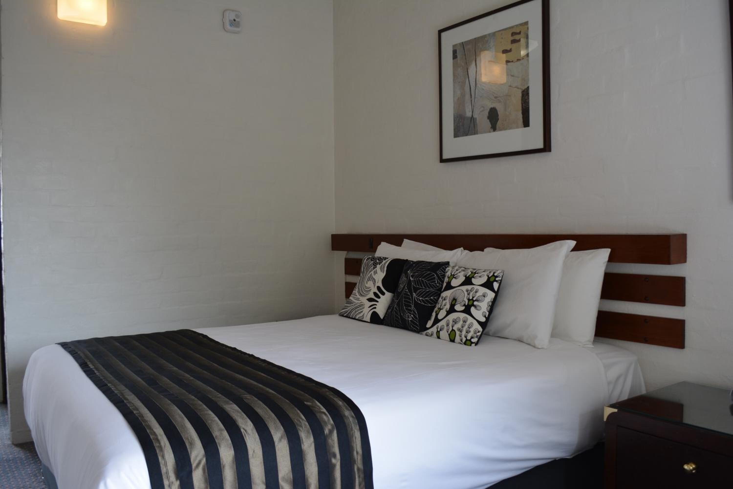 A neatly made bed with a striped blanket, white pillows, and a framed picture on the wall.