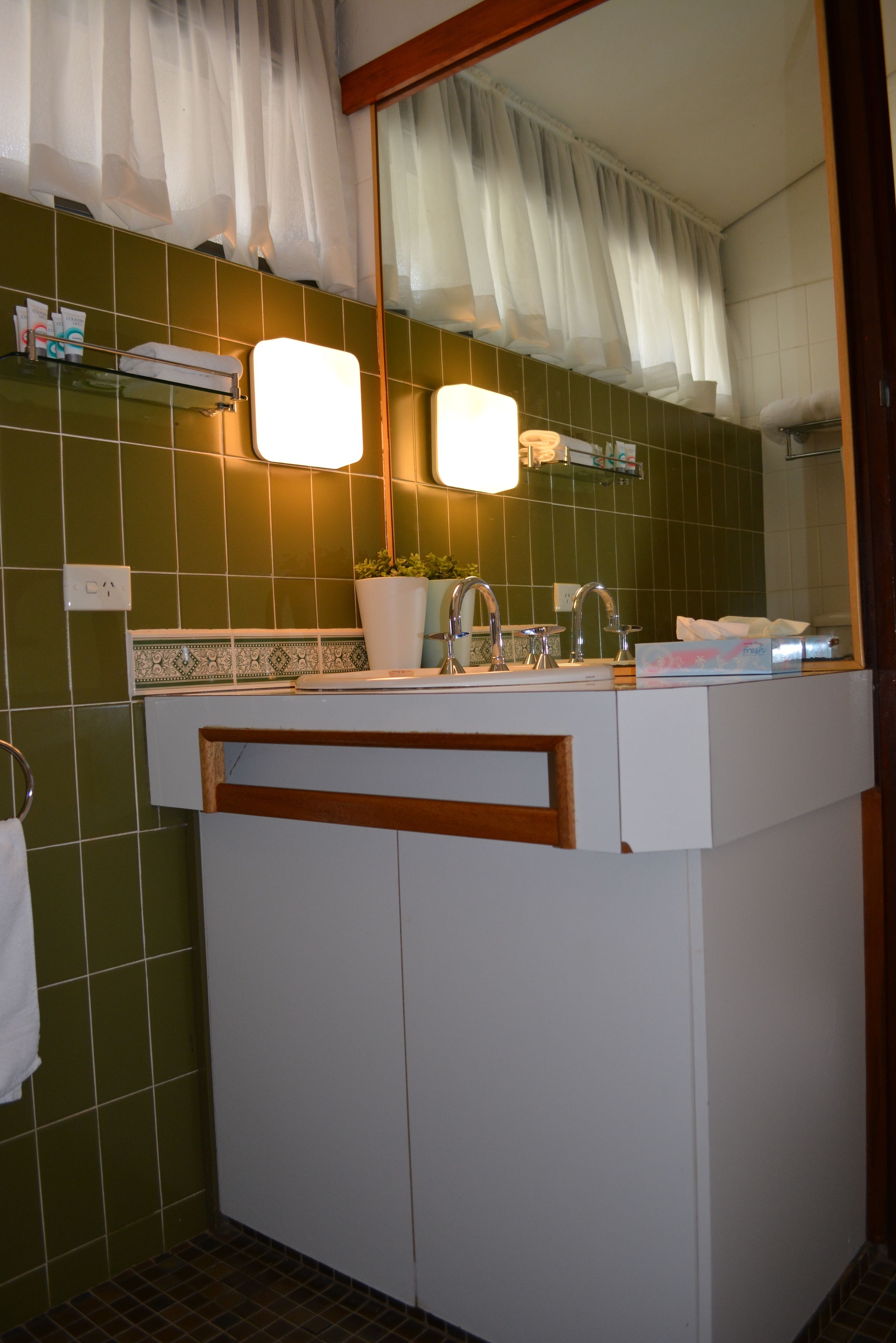 A bathroom with a white sink, green tiled walls, a mirror, and a potted plant.