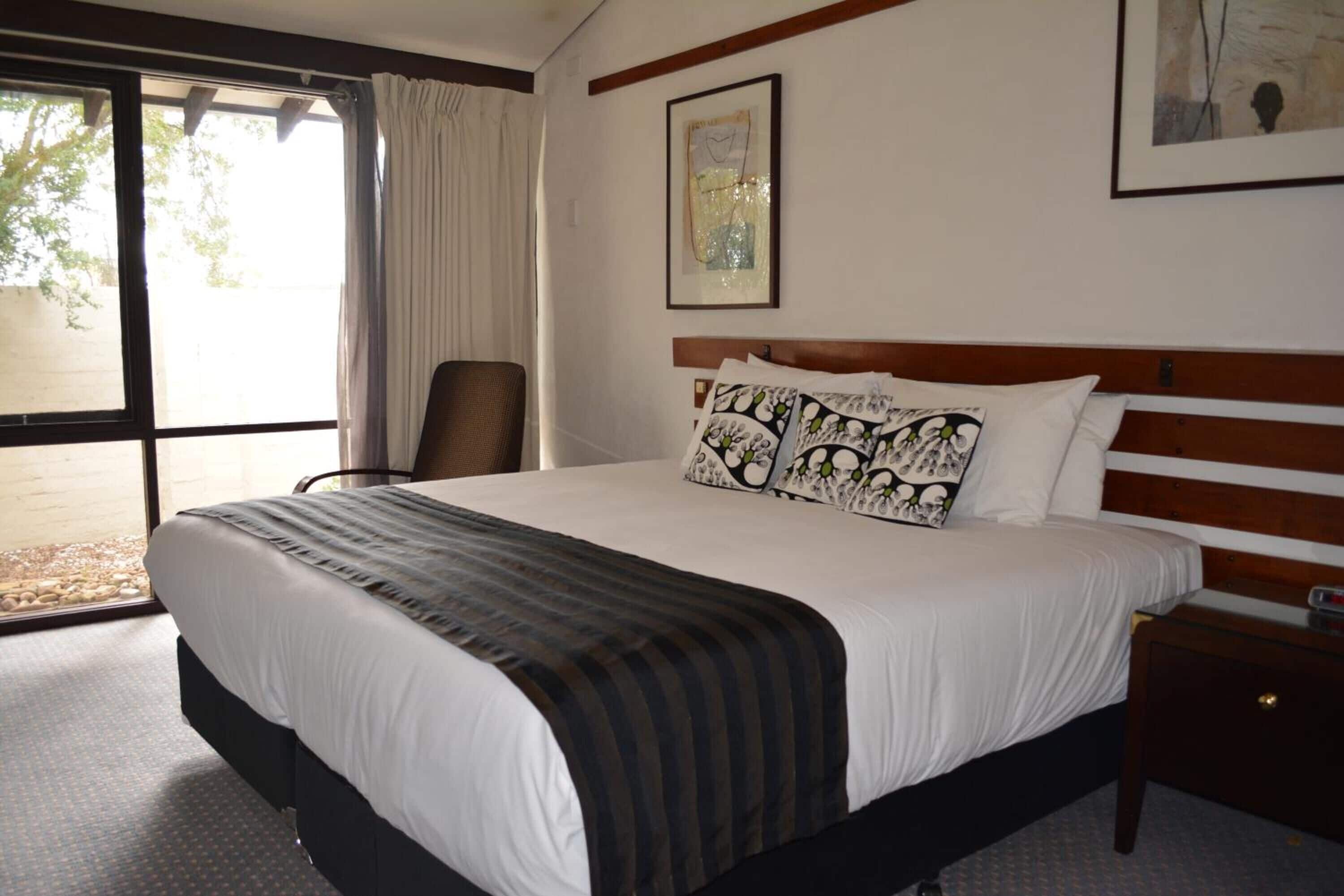 Una habitación de hotel con una cama grande, una silla, una mesita de noche y un ventanal con cortinas.