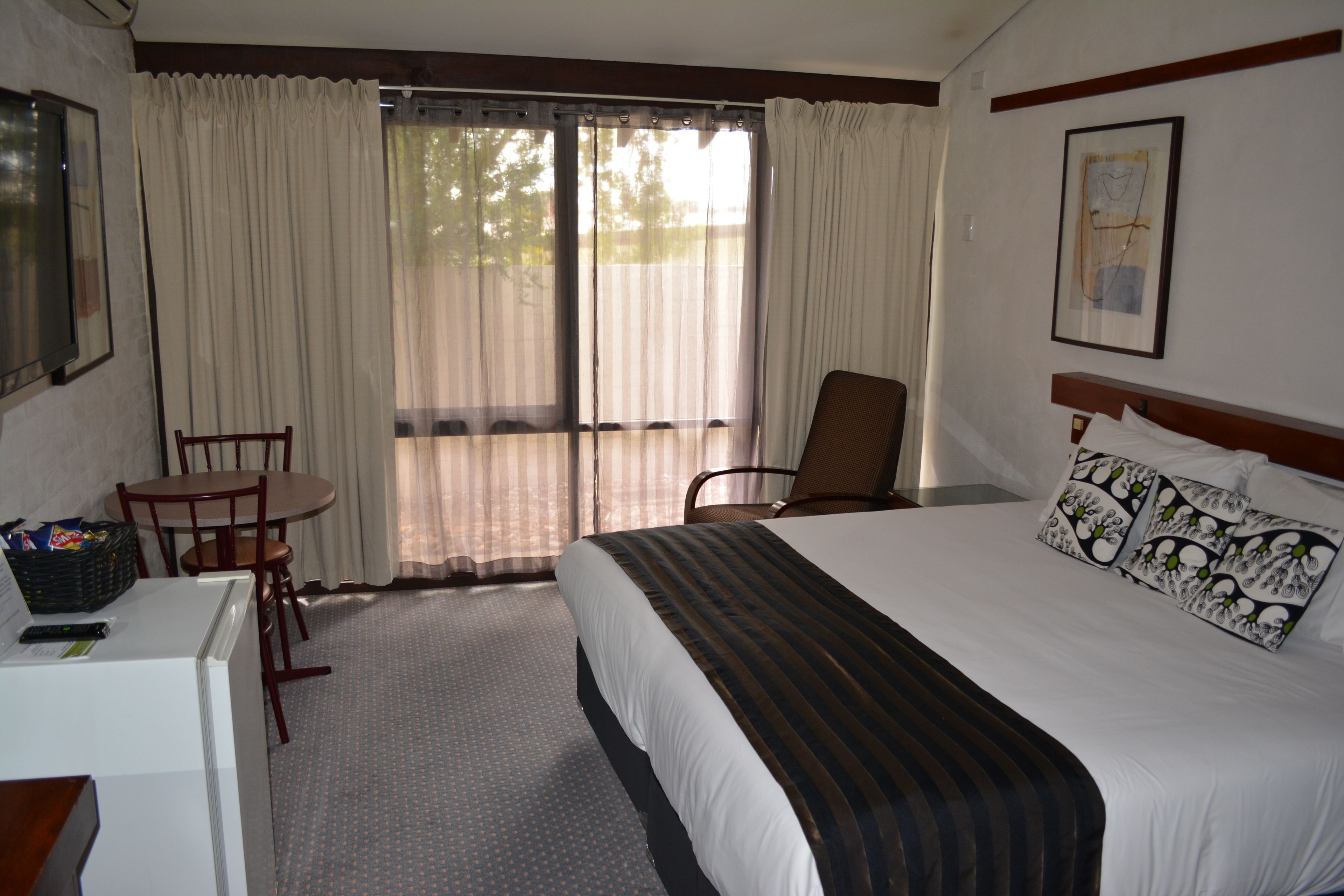 A hotel room with a bed, a desk, a chair, and a window with curtains.