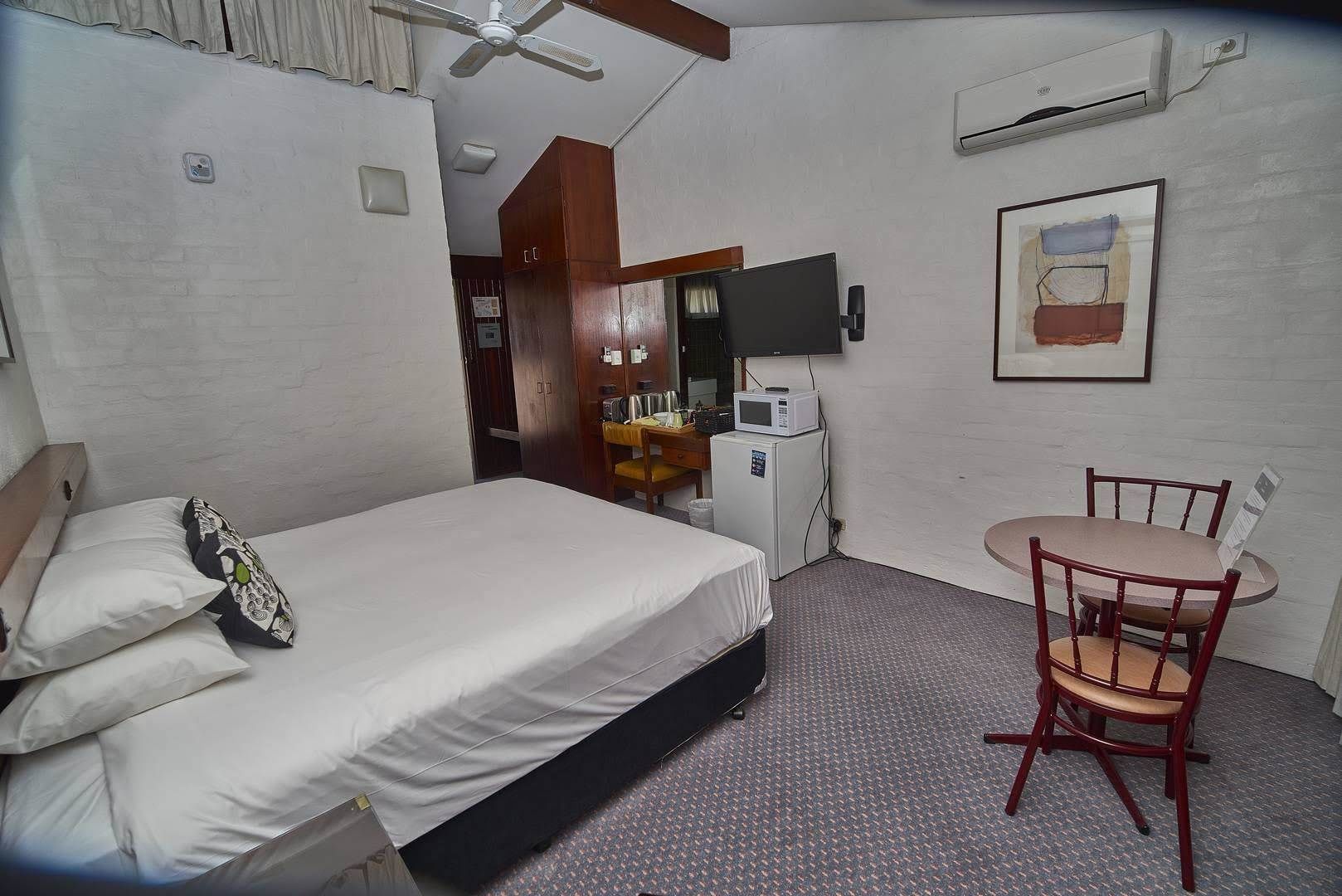 A hotel room with a bed, a desk with a chair, a microwave, and a television.