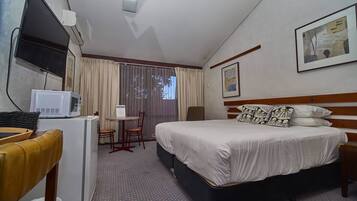 Habitación de hotel con cama, escritorio con silla, televisión, microondas y ventana con cortinas.