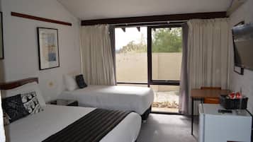 A hotel room with two beds, a small desk, a television, and a window with curtains.