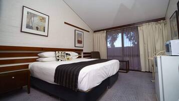Una camera d'albergo con un letto, una scrivania, una sedia, un forno a microonde e un frigorifero.