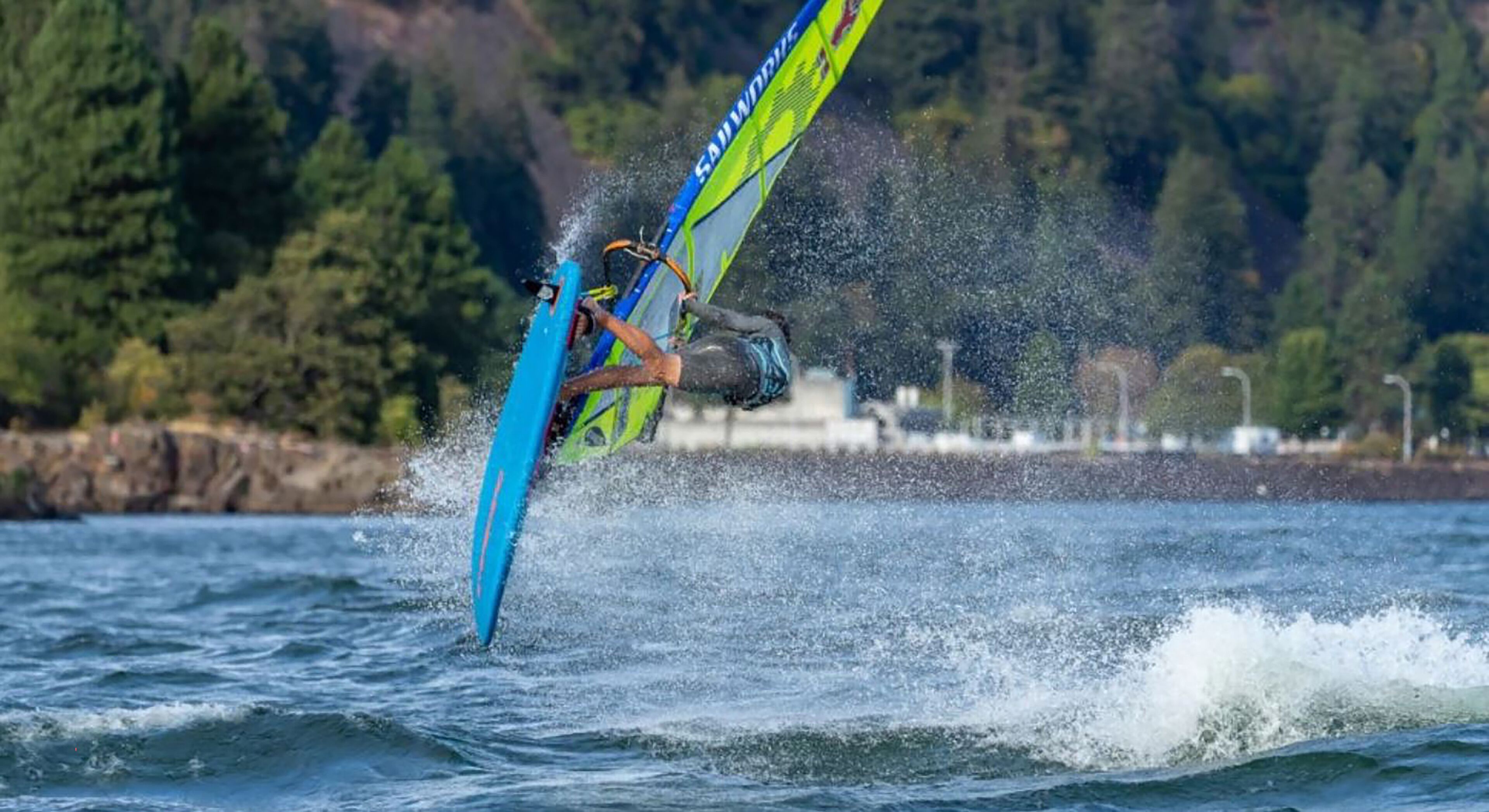 Eine Person windsurft auf dem Wasser mit freier Sicht auf die umliegende Landschaft.