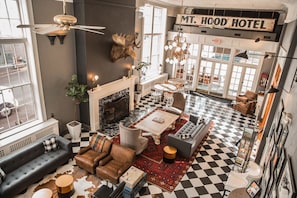 A spacious lobby with a checkered floor, a fireplace, and a sign reading "MT. HOOD HOTEL".