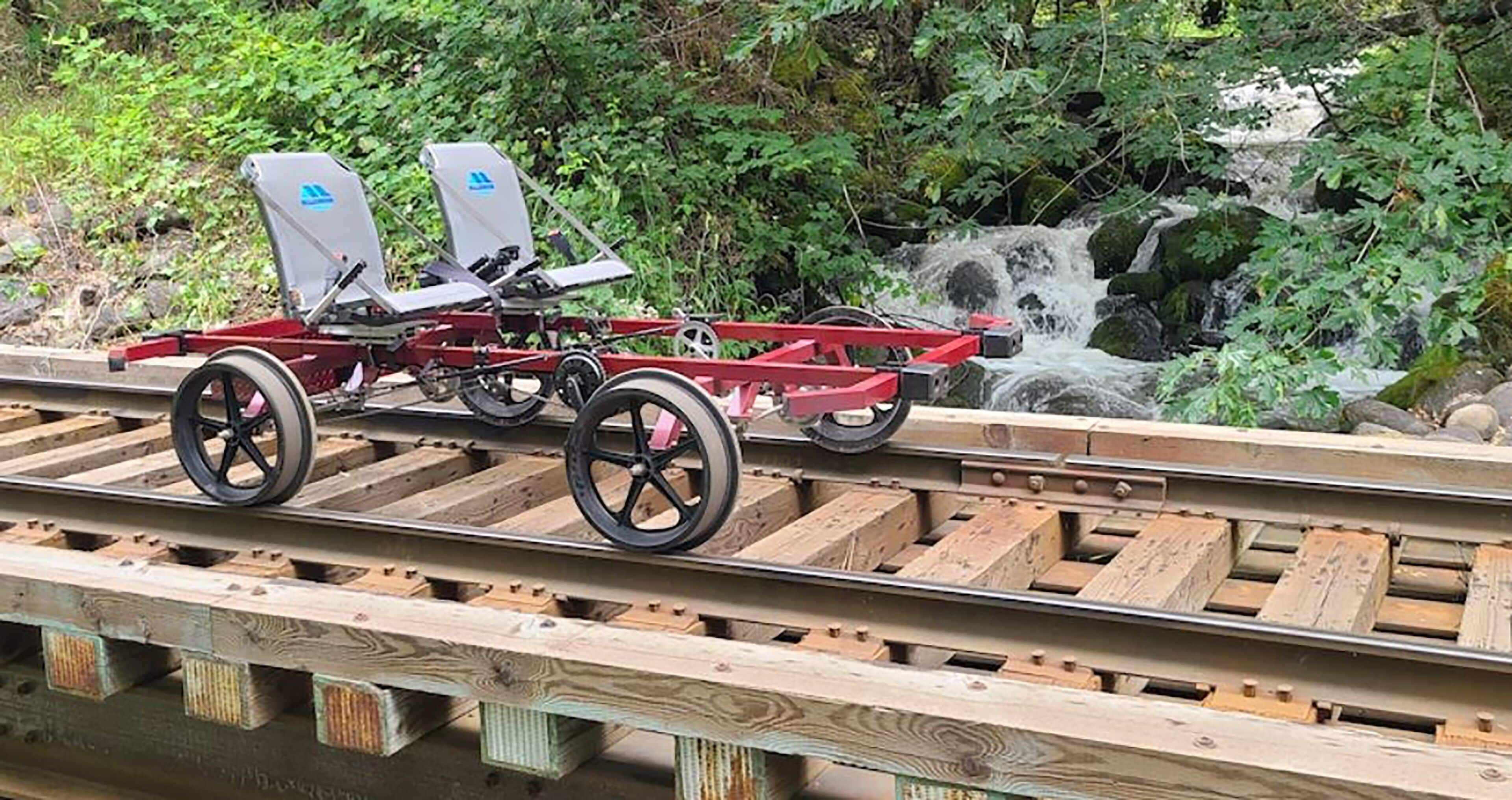 A wooden train track with a red train carriage and two seats.