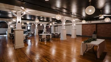 A spacious hall with wooden flooring, white pillars, and multiple tables and chairs.