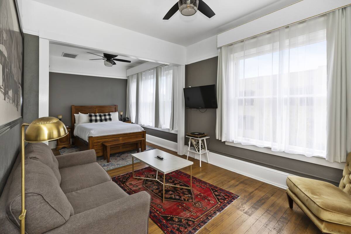 Moderni hotellihuone, jossa on sänky, sohva, sohvapöytä ja televisio.