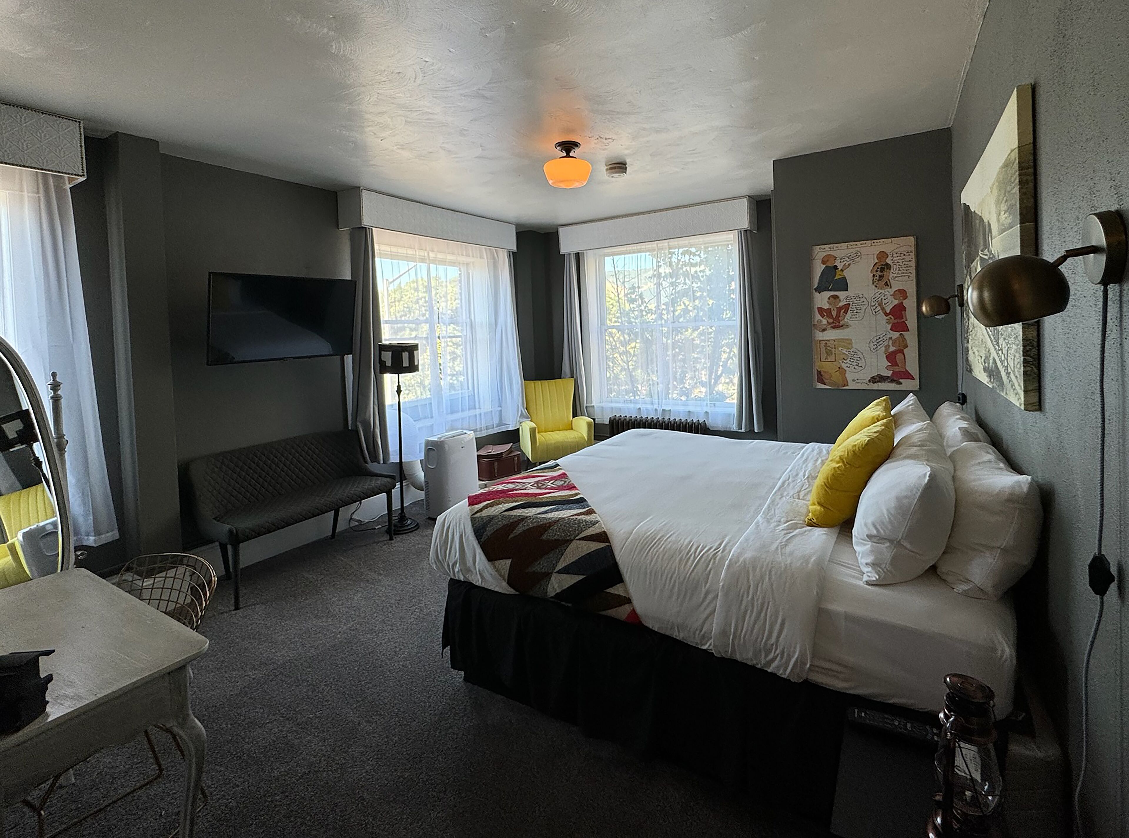 Habitación de hotel con una cama grande, un escritorio, una silla, un televisor montado en la pared y una ventana con cortinas.