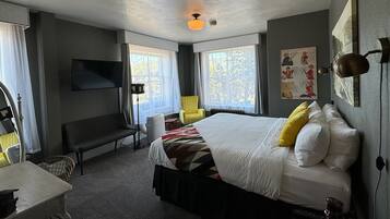 Habitación de hotel con una cama grande, un escritorio, una silla, un televisor montado en la pared y una ventana con cortinas.
