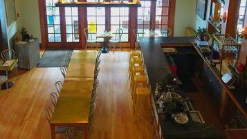 Un comedor espacioso con una larga mesa de madera y varias sillas, un área de bar con taburetes y ventanas amplias que dejan entrar luz natural.