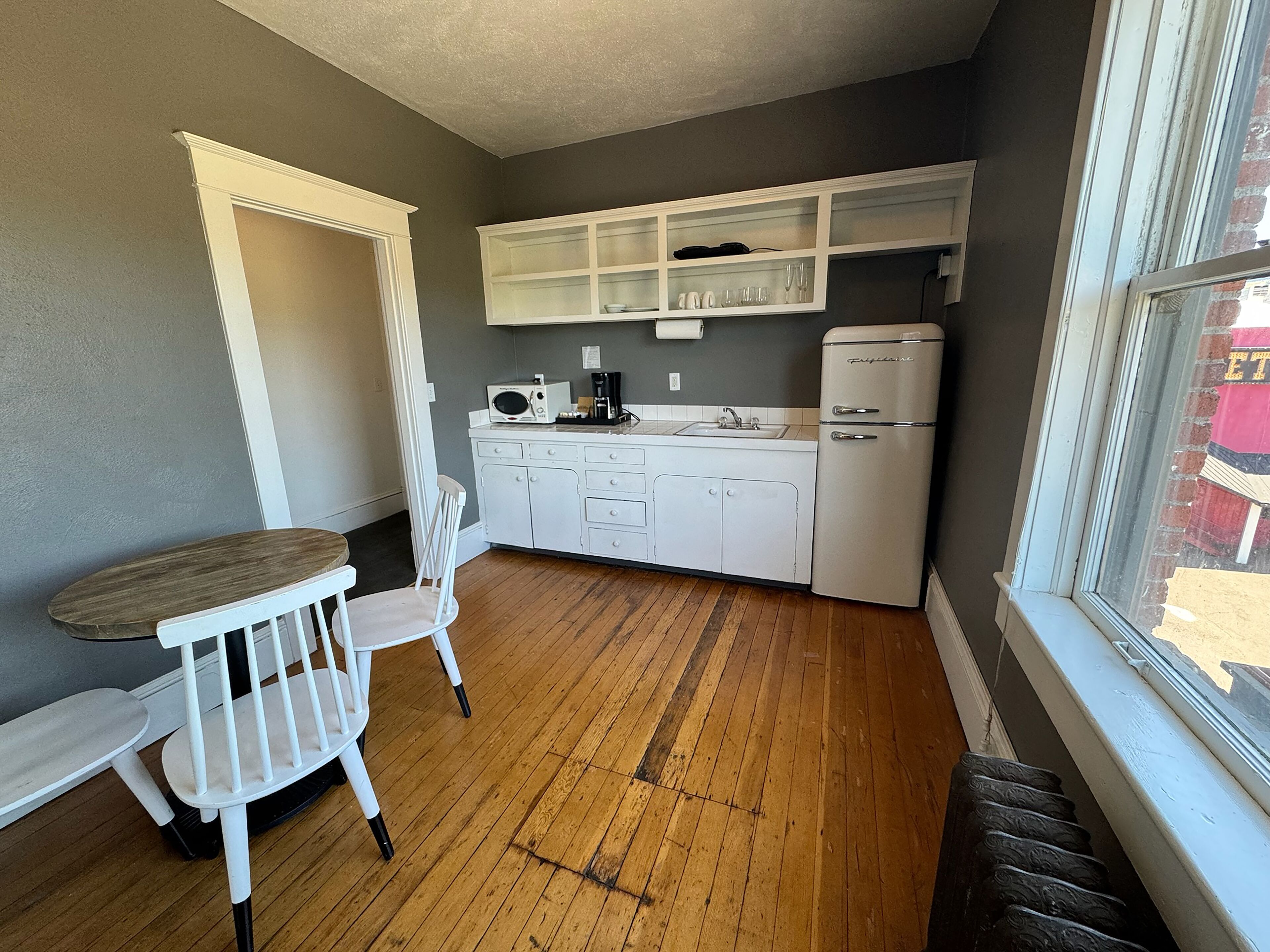 Una cocina compacta con muebles blancos, una mesa de comedor de madera y una silla.