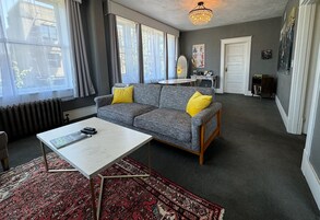 Una sala de estar con un sofá gris, cojines amarillos, una mesa de centro blanca y una alfombra estampada.