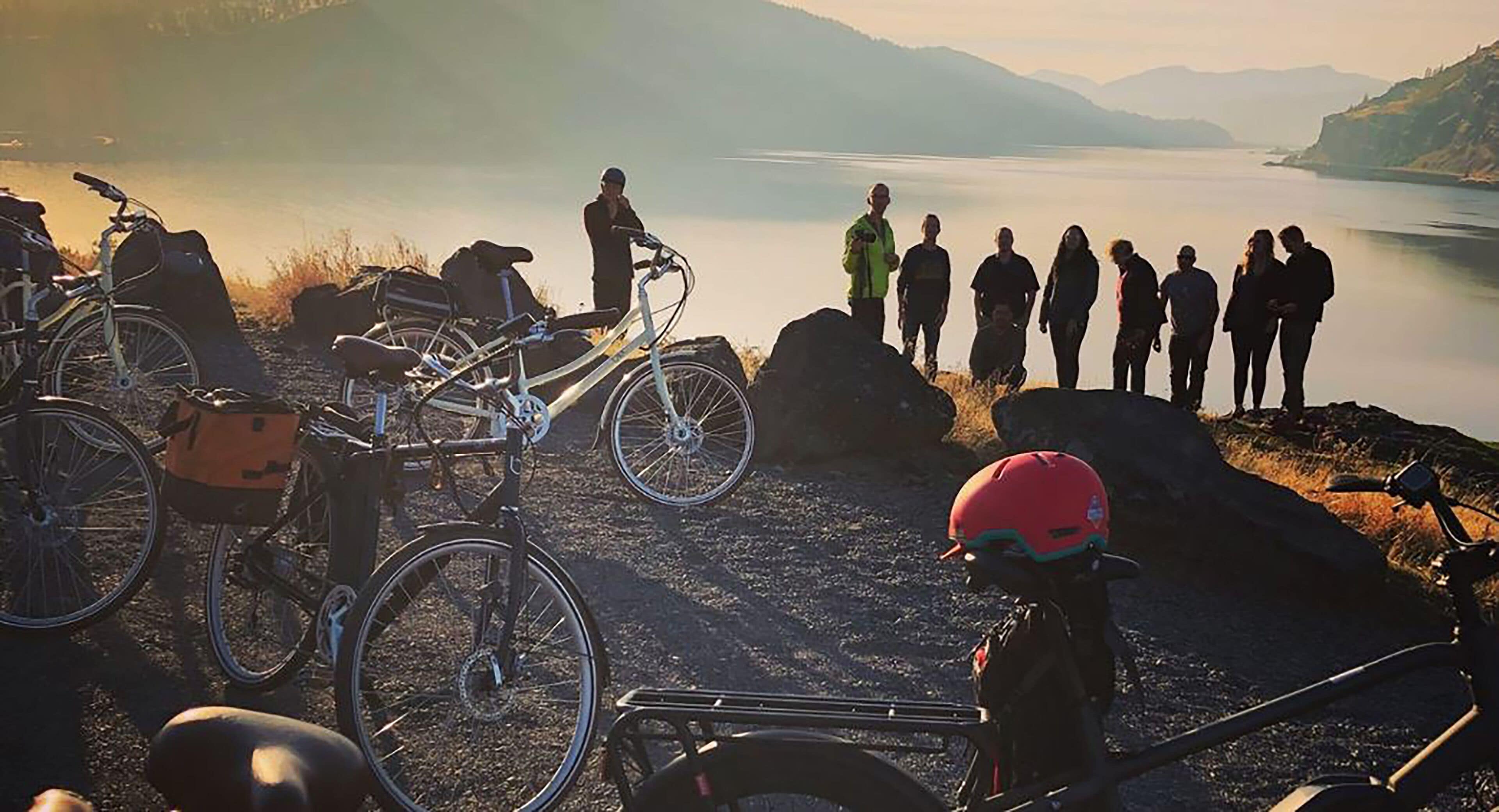 A group of people standing by a lake with bicycles and a dog nearby.