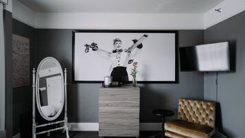 A room with a large framed picture, a mirror, a dresser, a tufted sofa, and a flat-screen TV.
