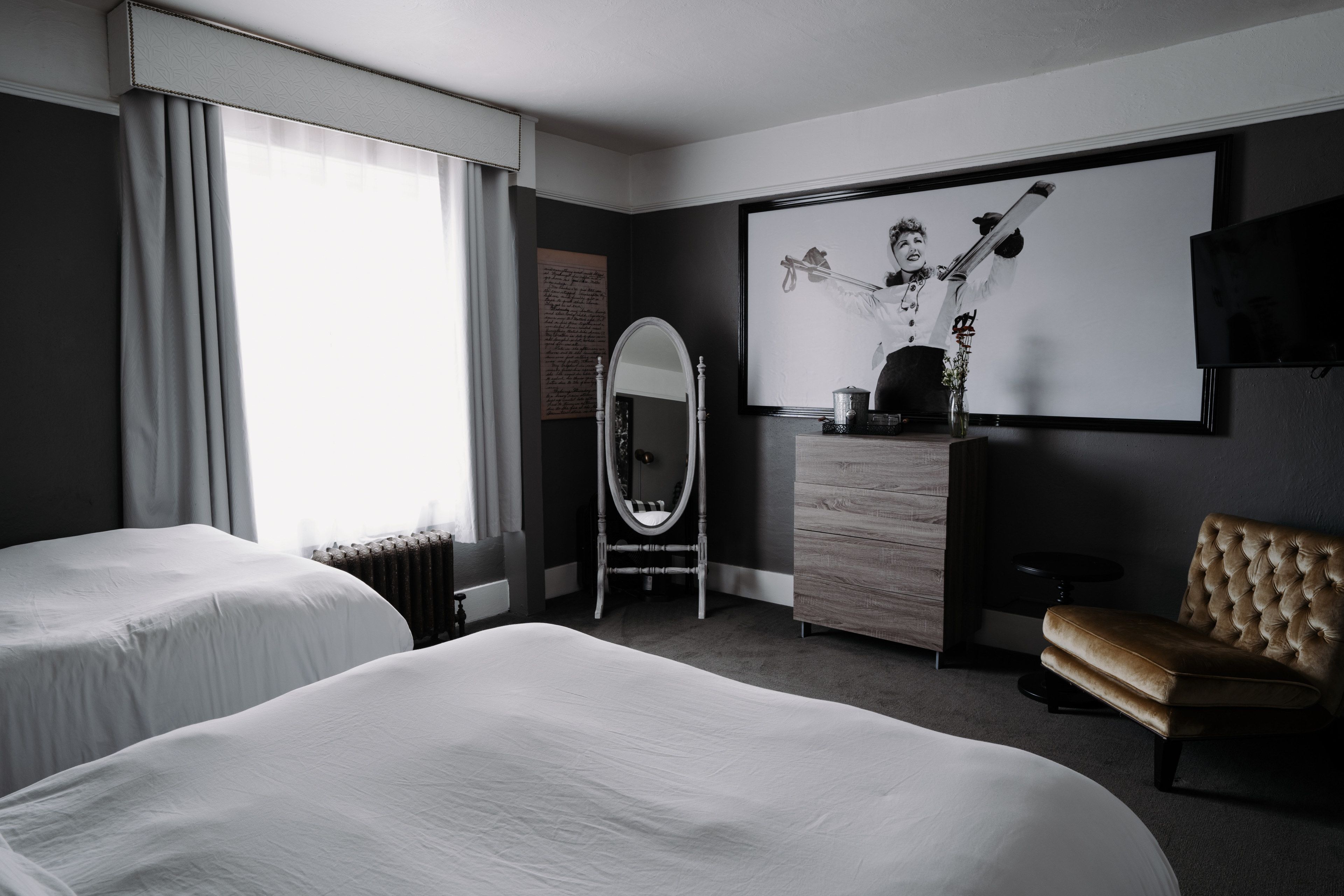 Habitación de hotel con dos camas, un espejo grande, un aparador, un televisor y un cuadro en la pared.