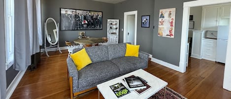 A living room with a grey sofa, yellow cushions, a coffee table with books, a ceiling fan, and a large framed picture on the wall.