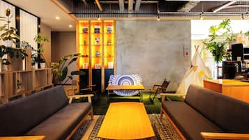 A cozy seating area with a central table, surrounded by sofas and chairs, with a decorative wall and plants in the background.