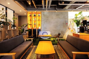 A cozy seating area with a central table, surrounded by sofas and chairs, with a decorative wall and plants in the background. - ArC LIFESTYLE SPACE & HOTEL (Mito)