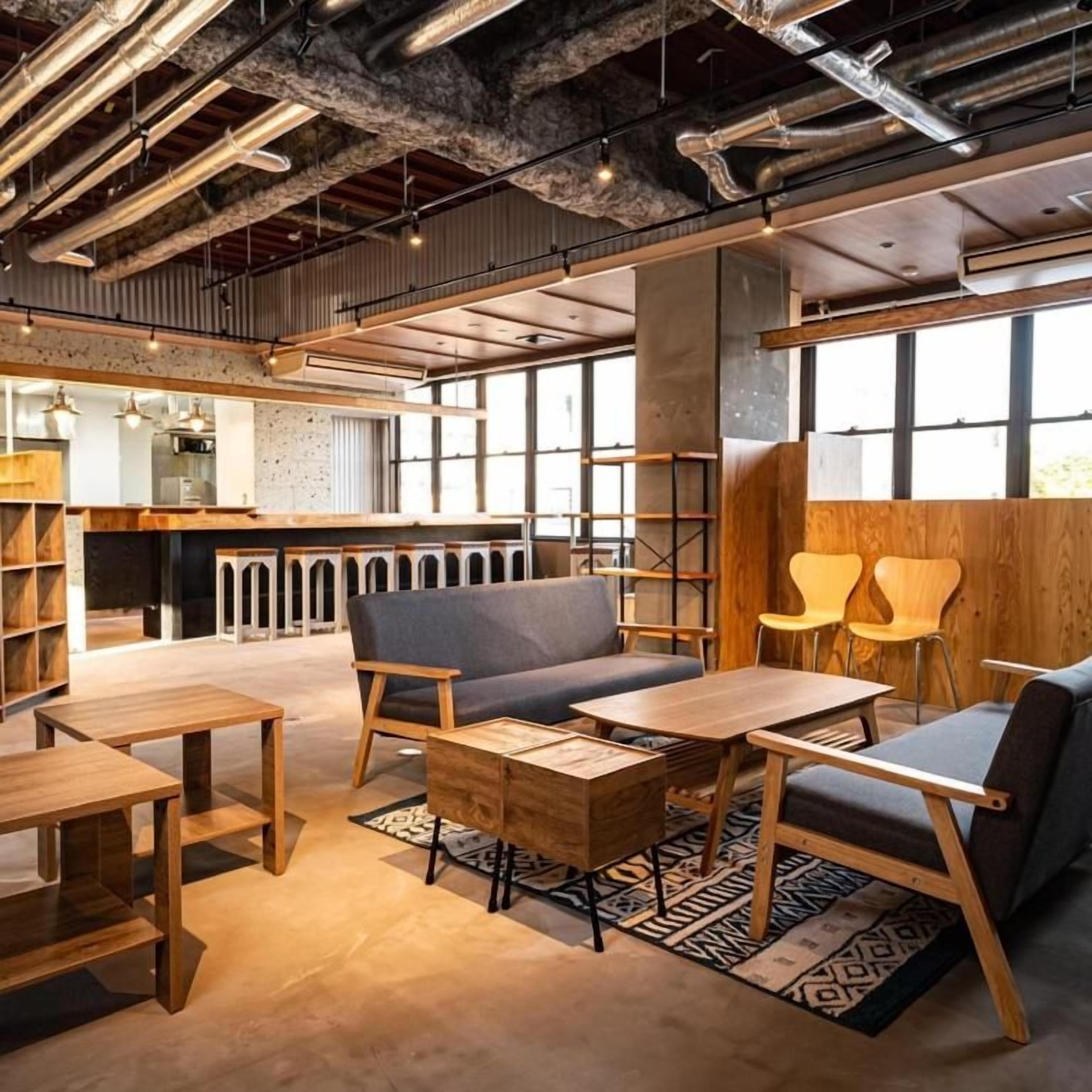 A modern interior with exposed ductwork, a bar area, seating, and a large window providing natural light.