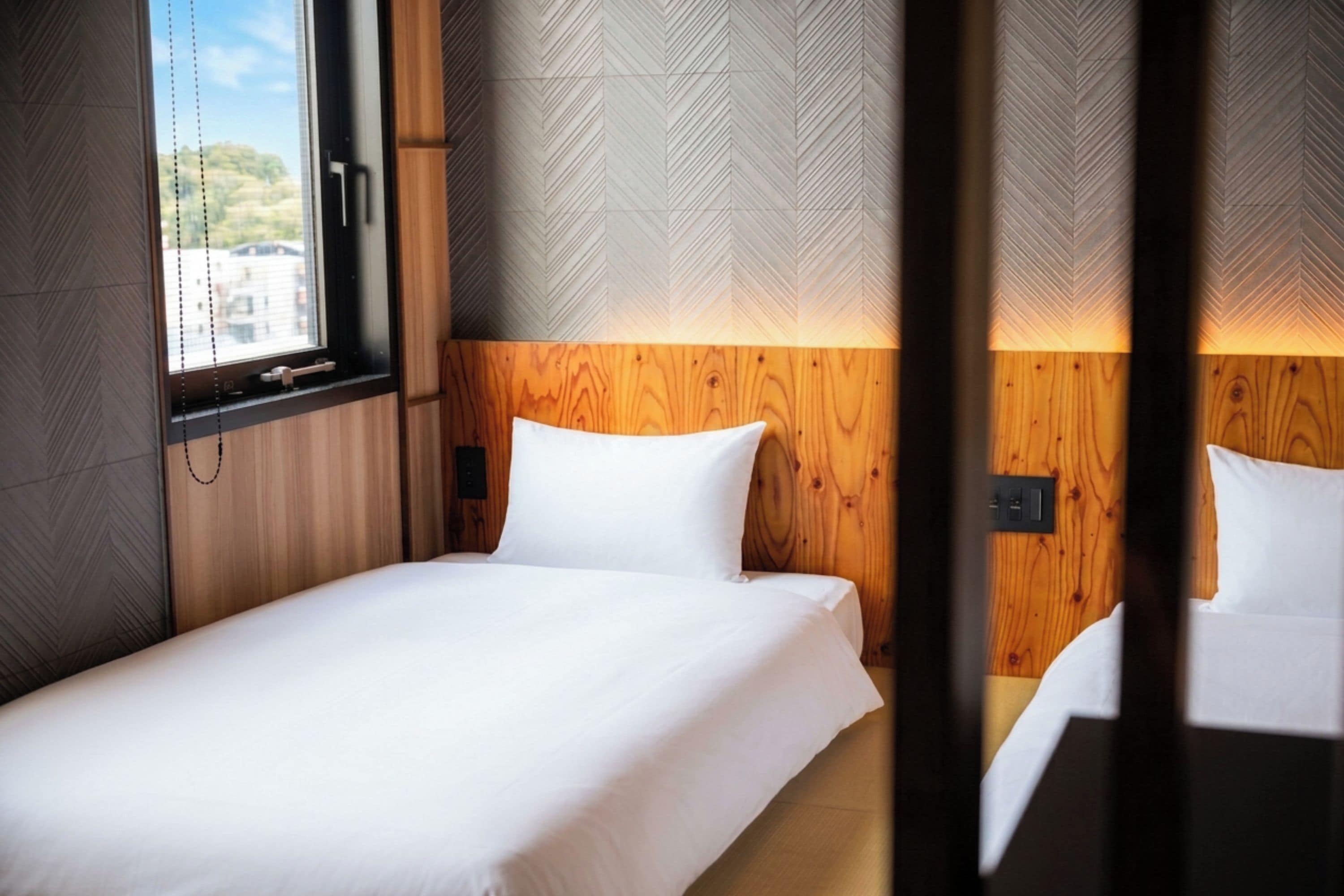 A hotel room with a bed, wooden headboard, and a window with blinds.