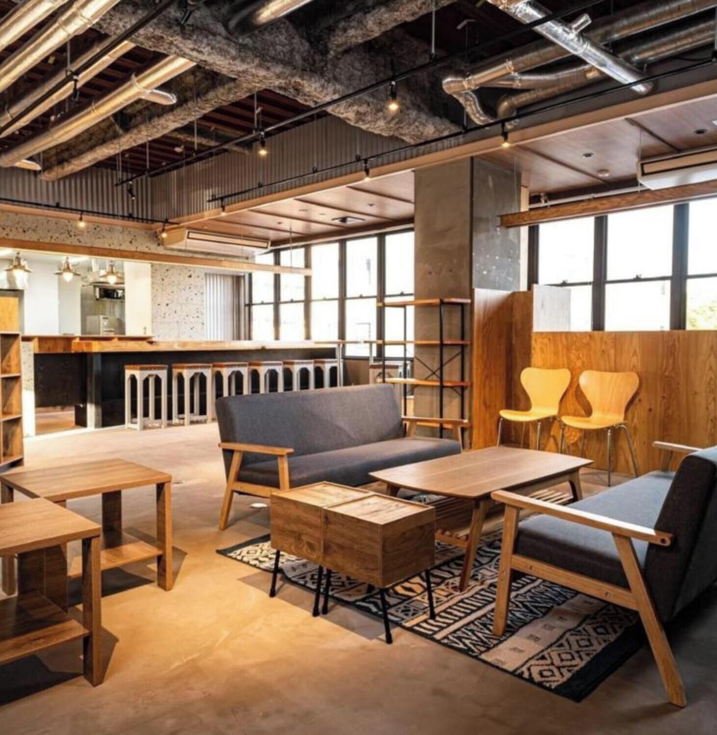 A modern interior with exposed ductwork, wooden furniture, and large windows.
