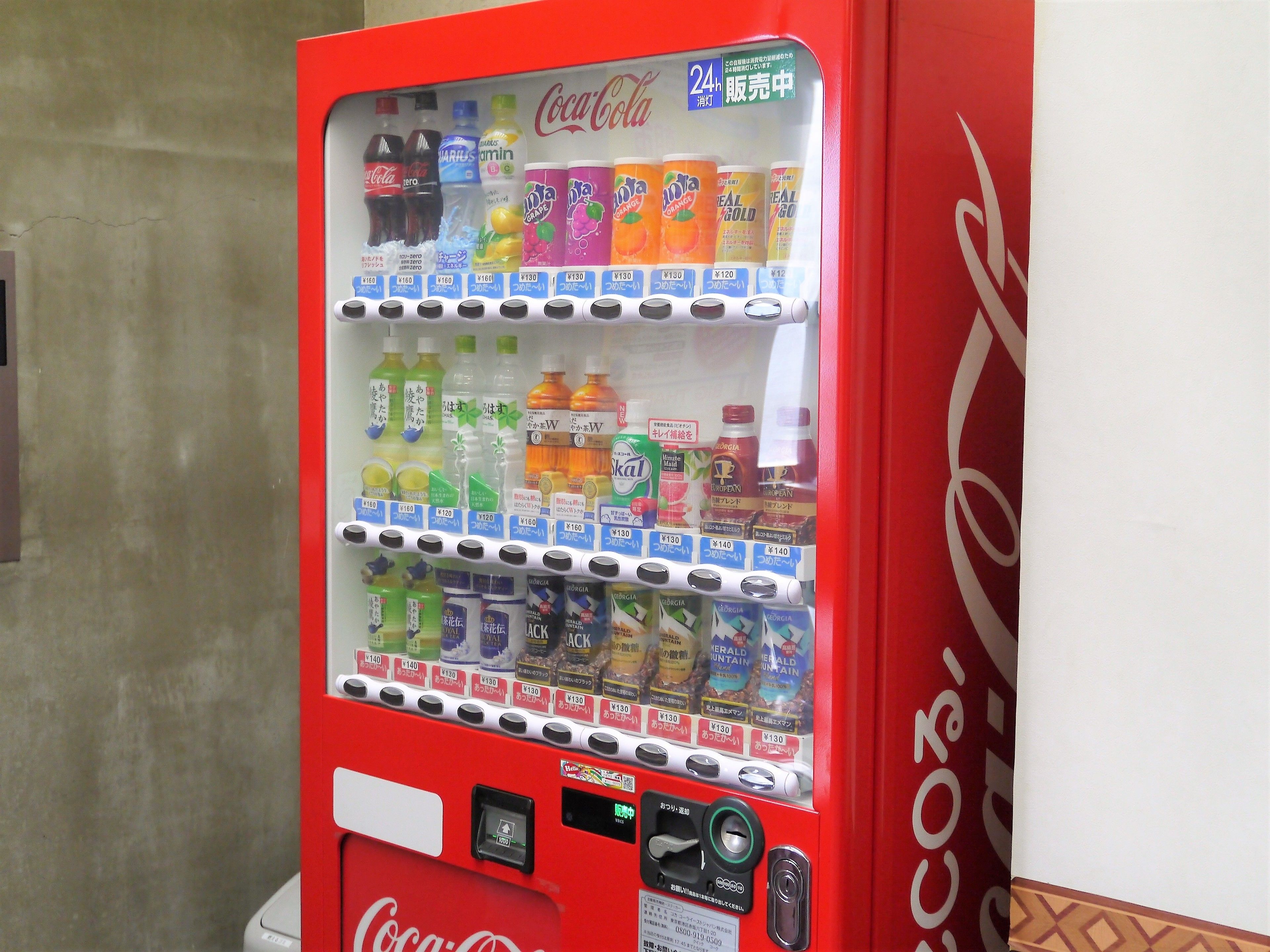 A vending machine with various drinks and snacks, including Coca-Cola, and a 24-hour service label.