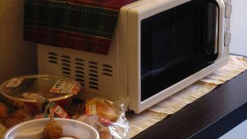 A microwave oven on a kitchen counter with a plaid cloth over it, a bowl of food, and some packaged food items.