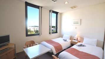 A hotel room with two beds, a desk, a chair, a television, and large windows offering a city view.