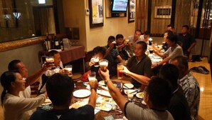 Un groupe de personnes est assis autour d’une table dans un restaurant, et un téléviseur est fixé au mur.