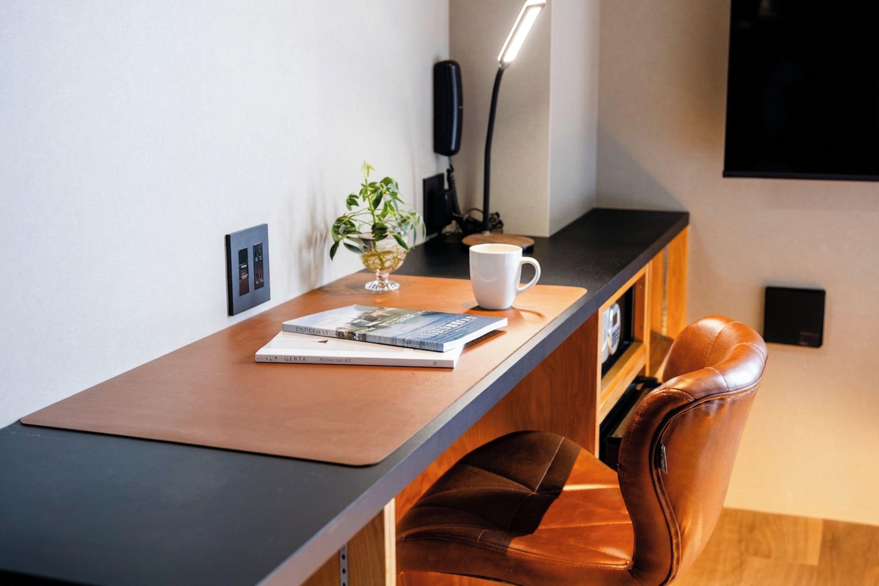 A modern workspace with a leather chair, a wooden desk, a white mug, a book, and a potted plant.