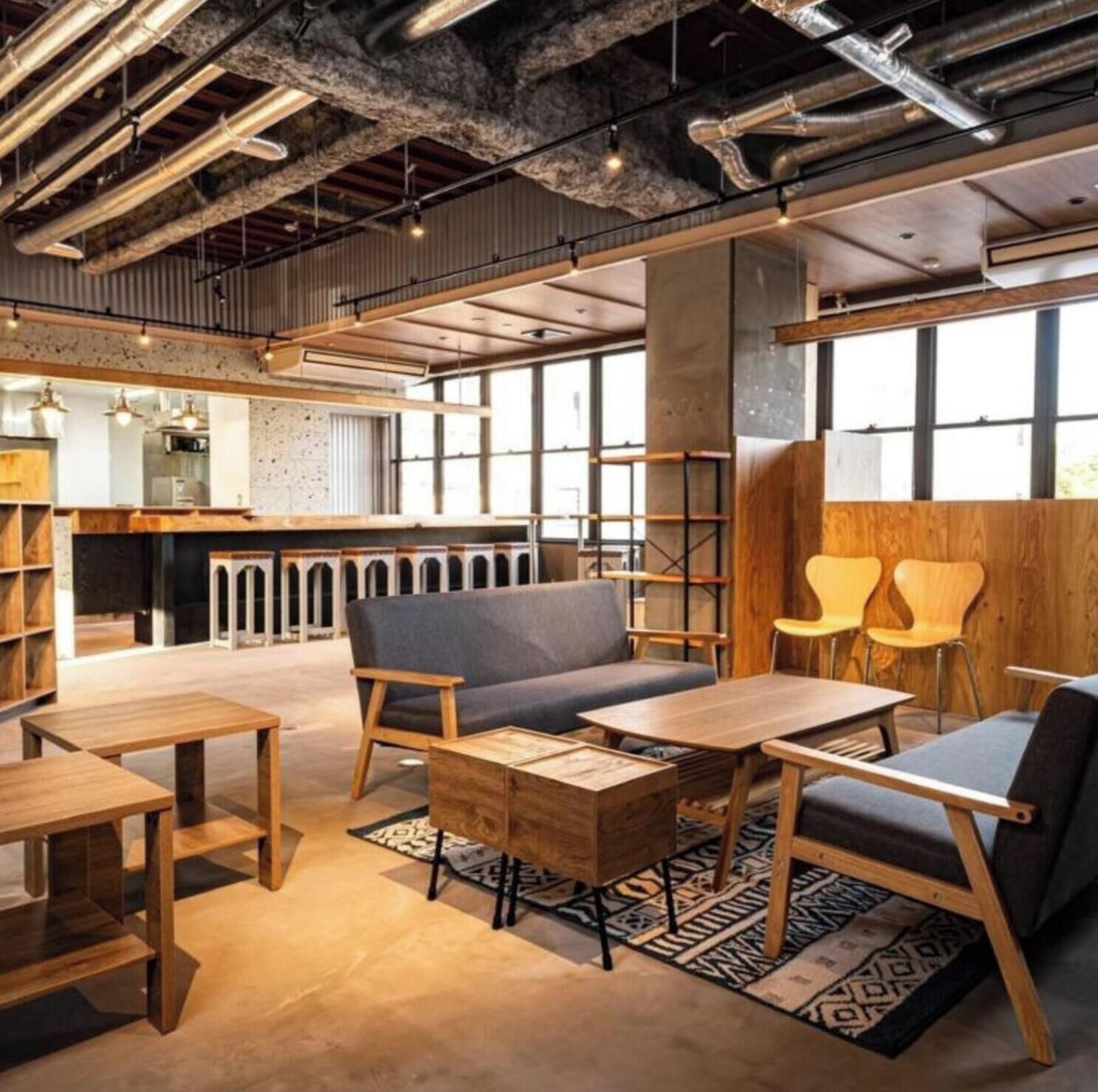 A modern interior with exposed ductwork, wooden furniture, and large windows.