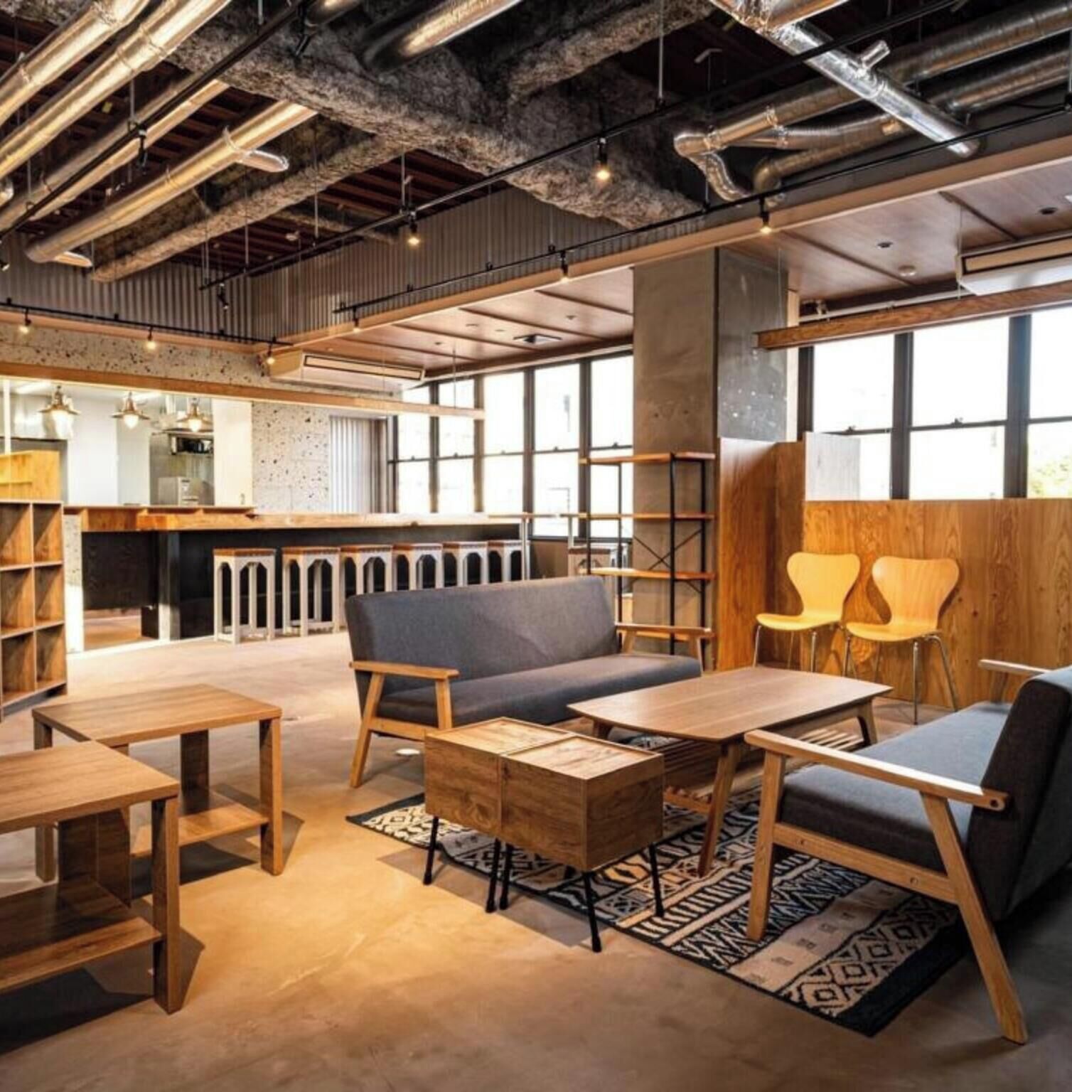 A modern interior with exposed ductwork, wooden furniture, and large windows.